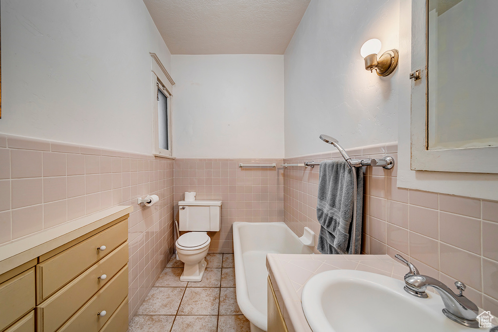 Bathroom featuring tile flooring, tile walls, a textured ceiling, sink, and toilet