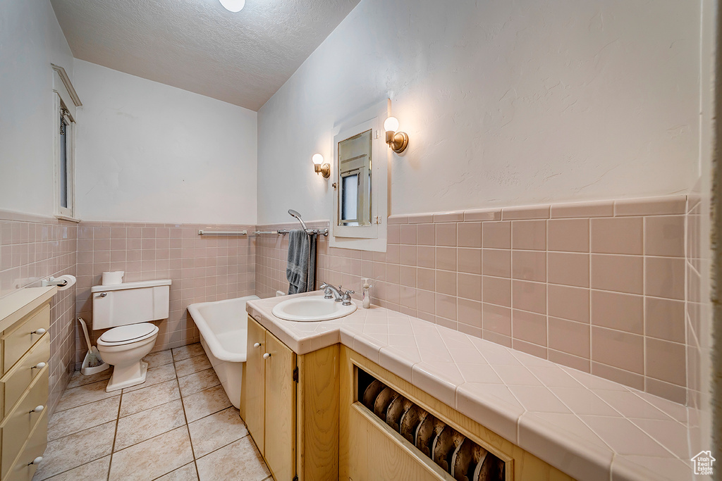 Bathroom with tile walls, toilet, tile floors, and a textured ceiling