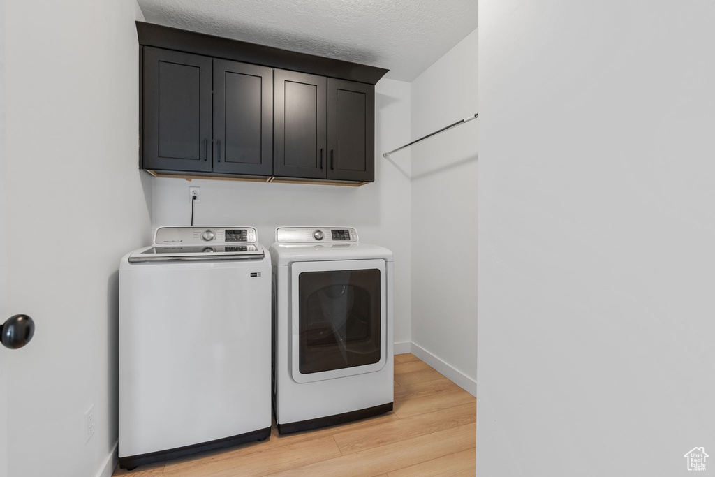 Laundry room with washing machine and dryer, cabinets, and light hardwood / wood-style floors