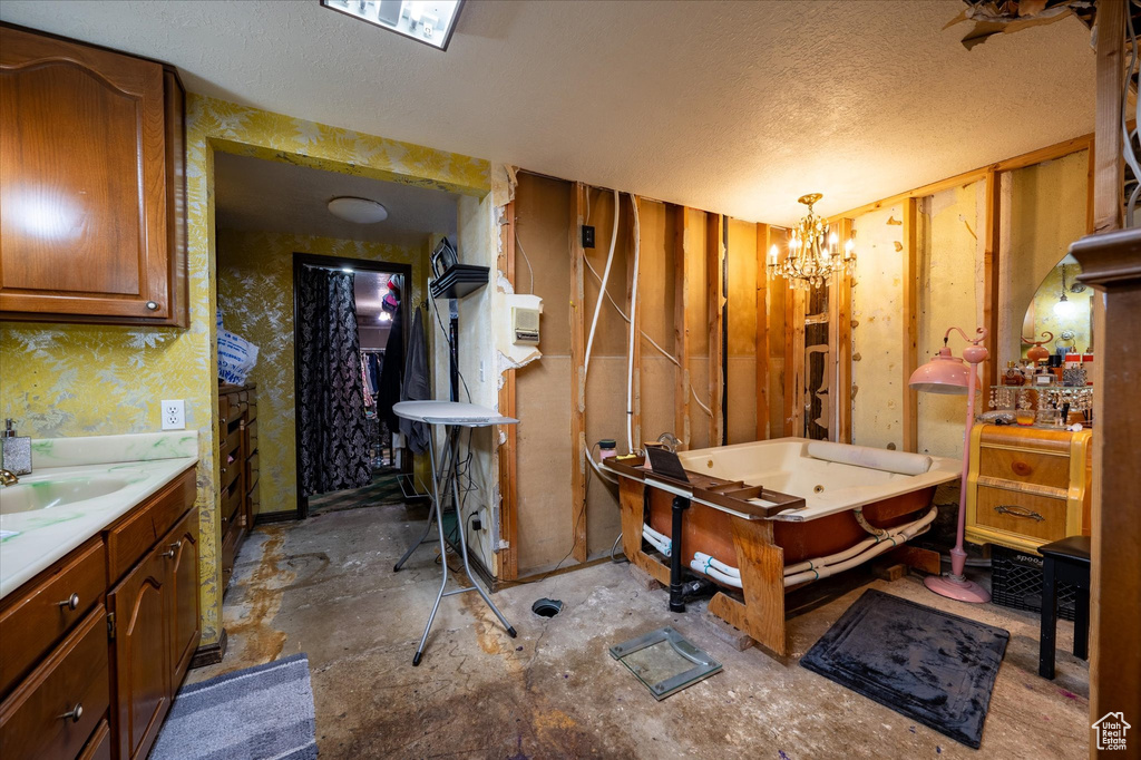 Bathroom with a bath, a notable chandelier, vanity, and a textured ceiling