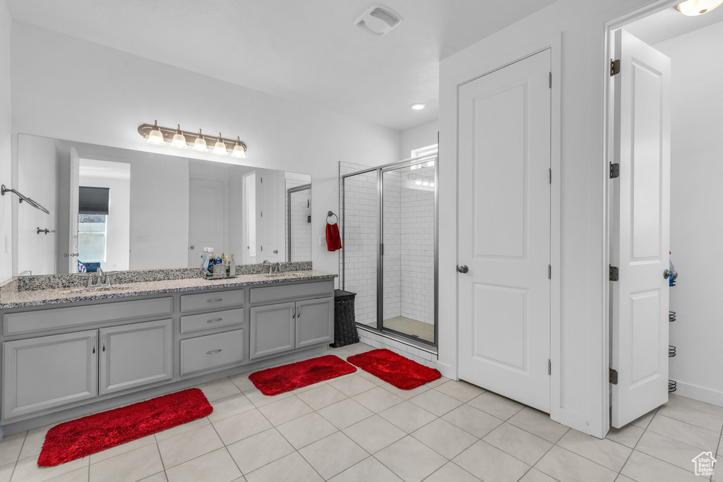 Bathroom featuring dual sinks, oversized vanity, tile floors, and a shower with shower door