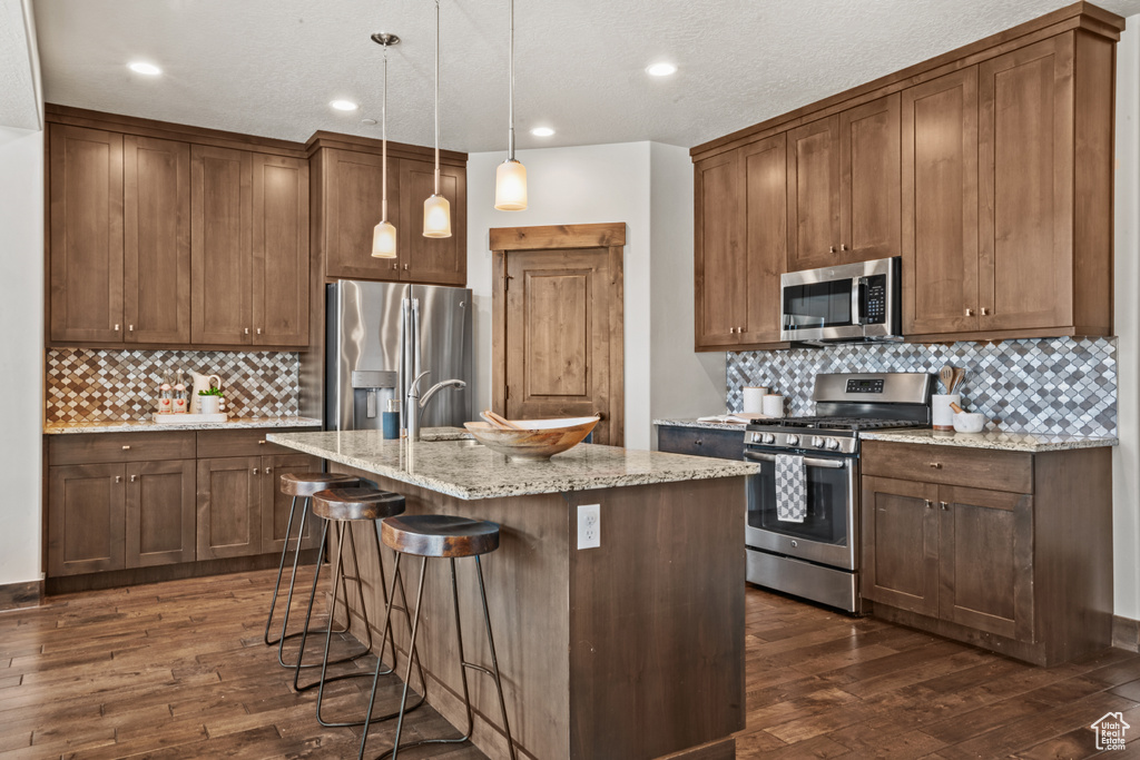 Kitchen featuring appliances with stainless steel finishes, tasteful backsplash, decorative light fixtures, dark hardwood / wood-style flooring, and a kitchen breakfast bar