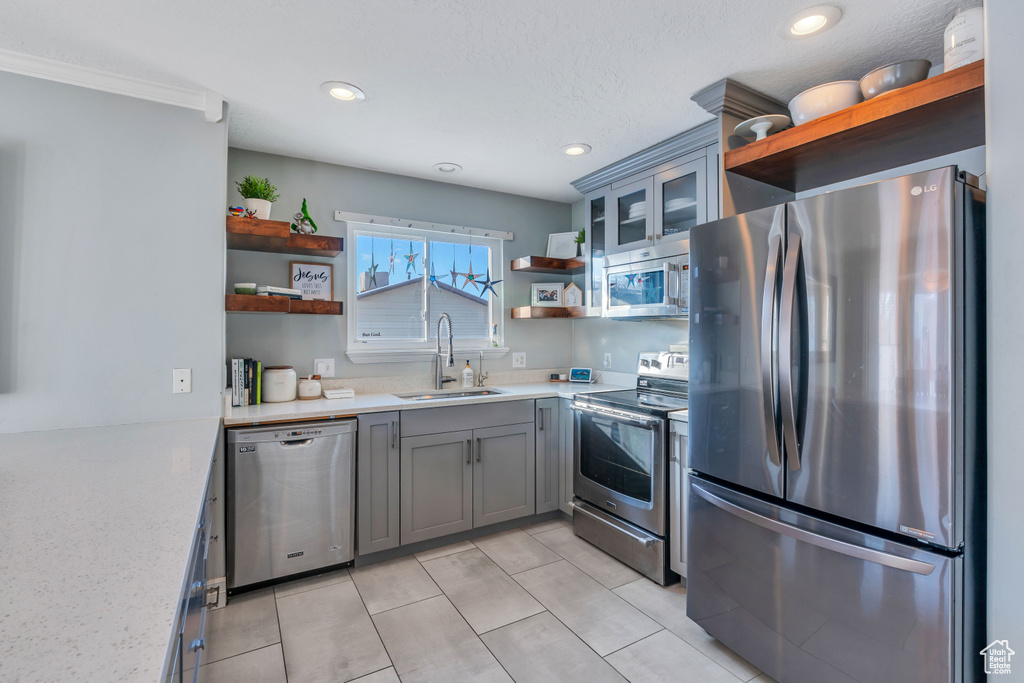 Kitchen featuring light tile floors, sink, gray cabinets, crown molding, and stainless steel appliances