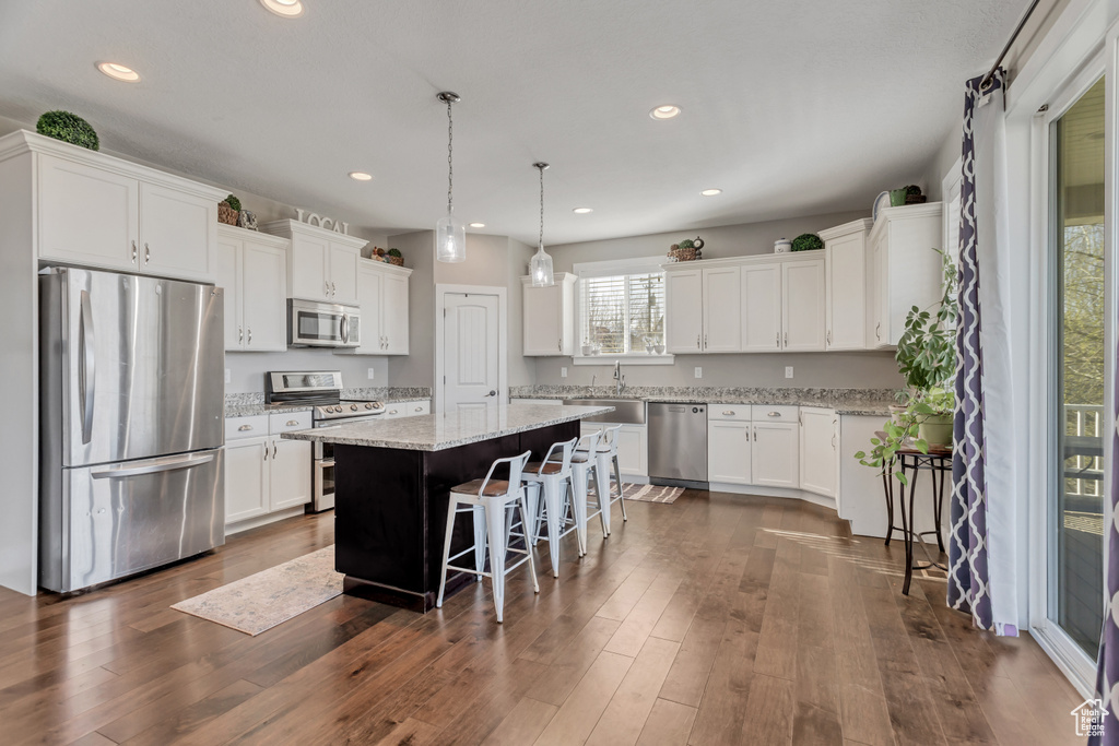 Kitchen featuring decorative light fixtures, appliances with stainless steel finishes, a kitchen bar, dark hardwood / wood-style floors, and a center island