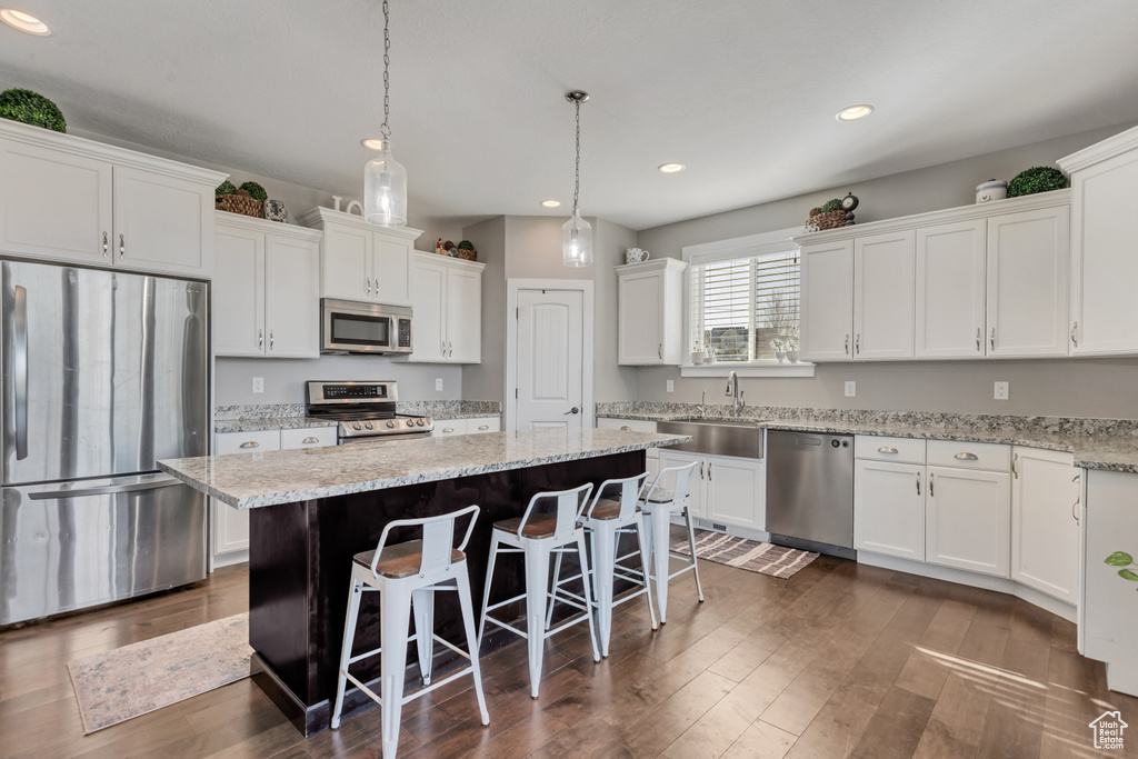 Kitchen featuring a kitchen breakfast bar, hanging light fixtures, dark hardwood / wood-style floors, appliances with stainless steel finishes, and a kitchen island