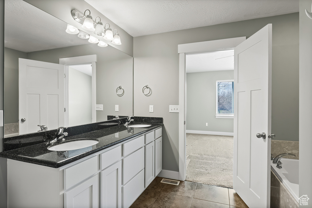Bathroom featuring tile flooring, double vanity, a relaxing tiled bath, and a textured ceiling
