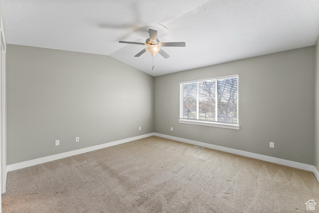 Spare room featuring light colored carpet, ceiling fan, and vaulted ceiling