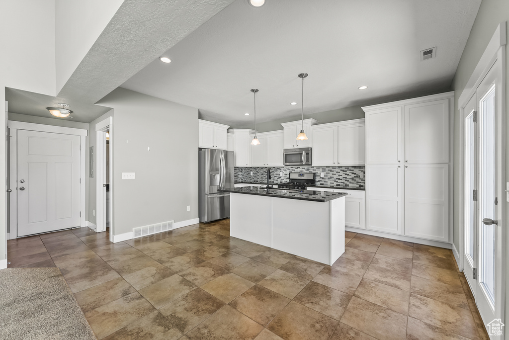 Kitchen featuring decorative light fixtures, appliances with stainless steel finishes, tasteful backsplash, white cabinets, and a center island