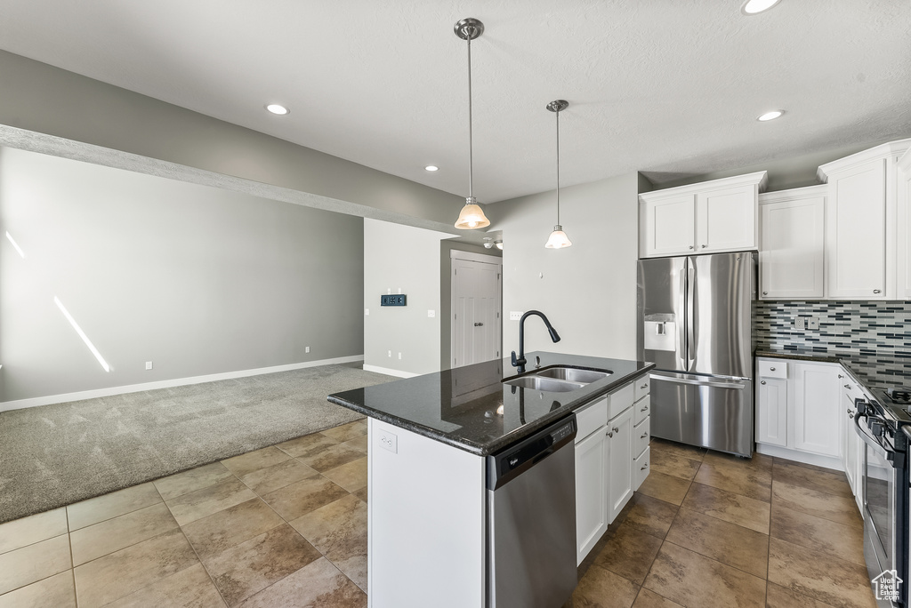 Kitchen featuring pendant lighting, light carpet, backsplash, stainless steel appliances, and a kitchen island with sink