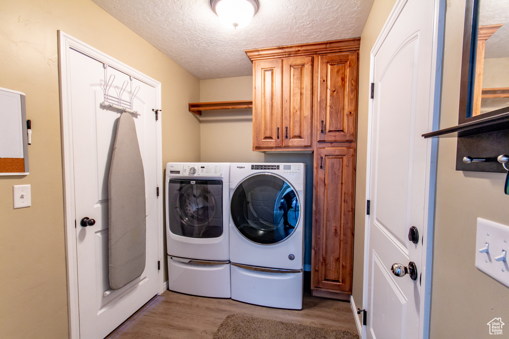 Laundry area with cabinets, light hardwood / wood-style floors, a textured ceiling, and washing machine and clothes dryer