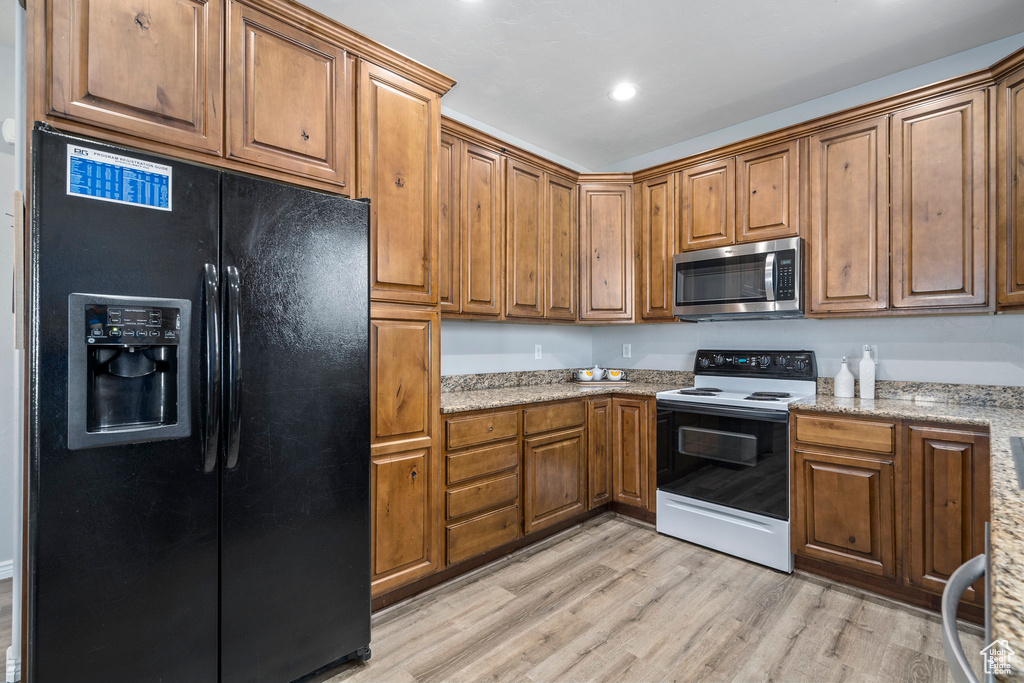 Kitchen with light hardwood / wood-style flooring, electric range, black fridge, and light stone counters