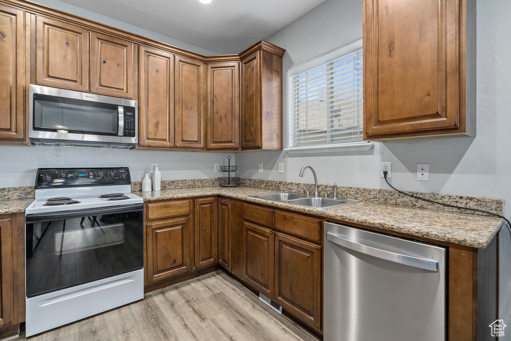 Kitchen with sink, light hardwood / wood-style floors, stainless steel appliances, and light stone countertops