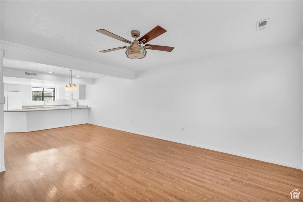 Unfurnished living room featuring crown molding, light hardwood / wood-style flooring, ceiling fan, and sink