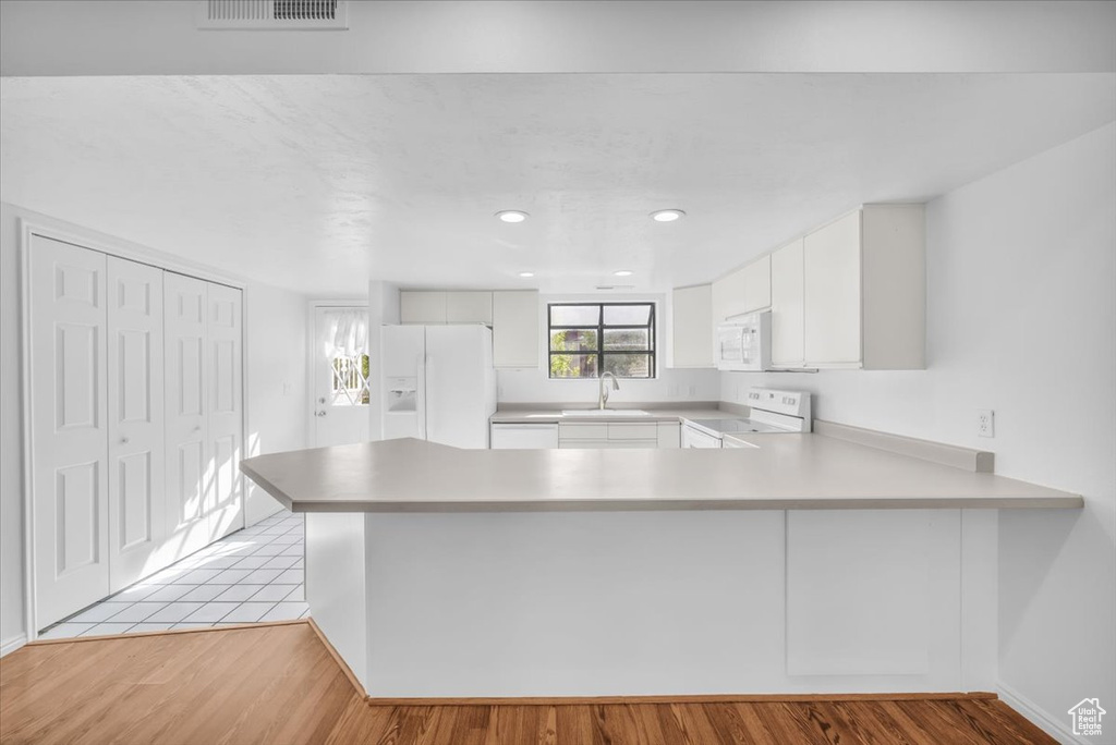 Kitchen featuring white cabinets, sink, white appliances, light wood-type flooring, and kitchen peninsula