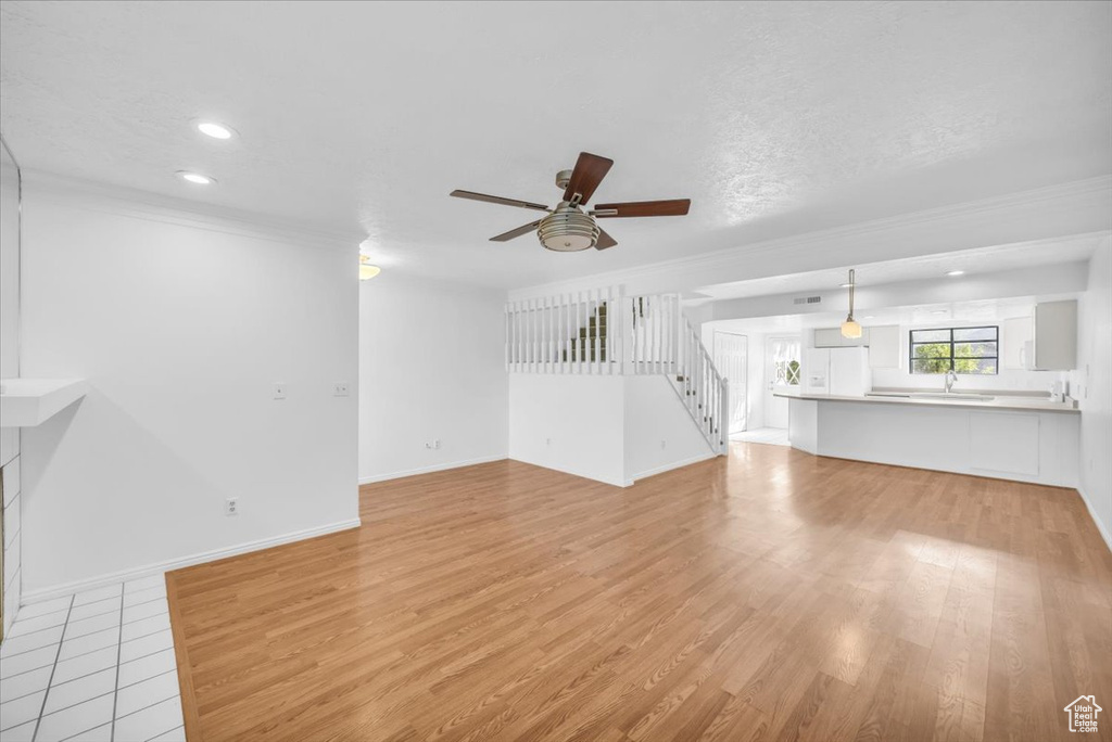 Unfurnished living room with ornamental molding, sink, light hardwood / wood-style flooring, and ceiling fan