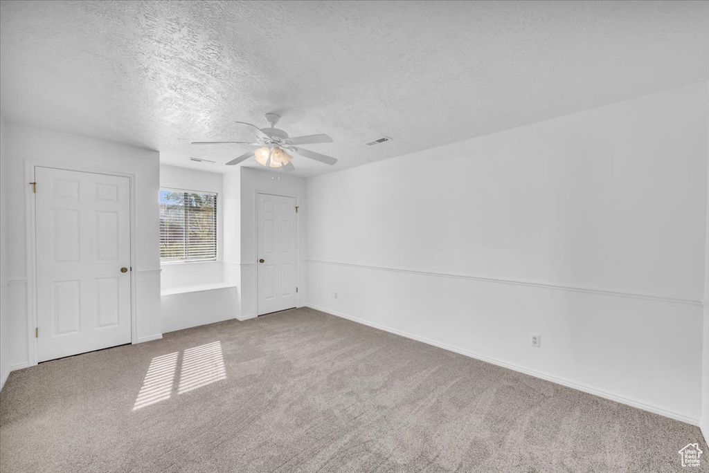 Empty room featuring carpet flooring, ceiling fan, and a textured ceiling