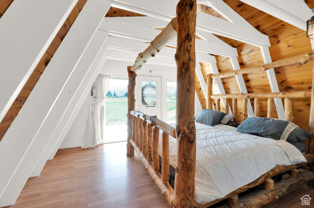 Bedroom with lofted ceiling with beams, light hardwood / wood-style floors, and access to exterior