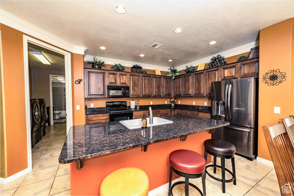 Kitchen featuring black appliances, independent washer and dryer, a kitchen island with sink, a kitchen breakfast bar, and sink
