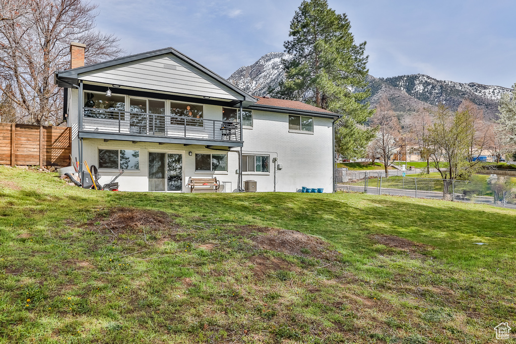 Rear view of property featuring a mountain view, a balcony, and a lawn