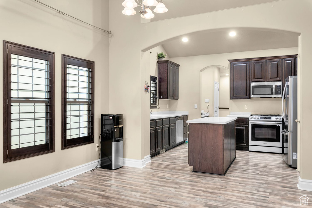 Kitchen with appliances with stainless steel finishes, light hardwood / wood-style flooring, dark brown cabinetry, and a kitchen island