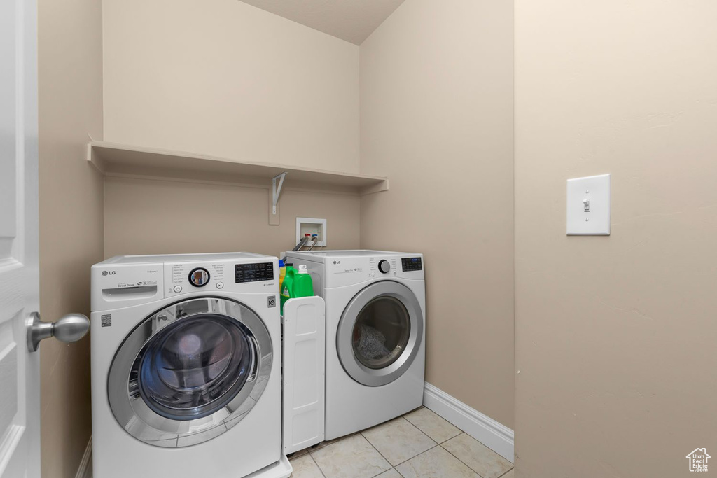 Clothes washing area with light tile flooring, washer hookup, and washer and clothes dryer