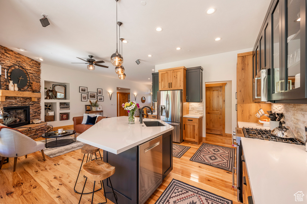 Kitchen with backsplash, appliances with stainless steel finishes, ceiling fan, light hardwood / wood-style floors, and a fireplace