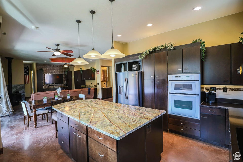 Kitchen featuring white double oven, ceiling fan, a kitchen island, stainless steel refrigerator with ice dispenser, and light stone countertops