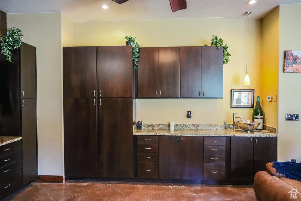 Kitchen featuring dark brown cabinetry, light stone counters, and dark tile floors