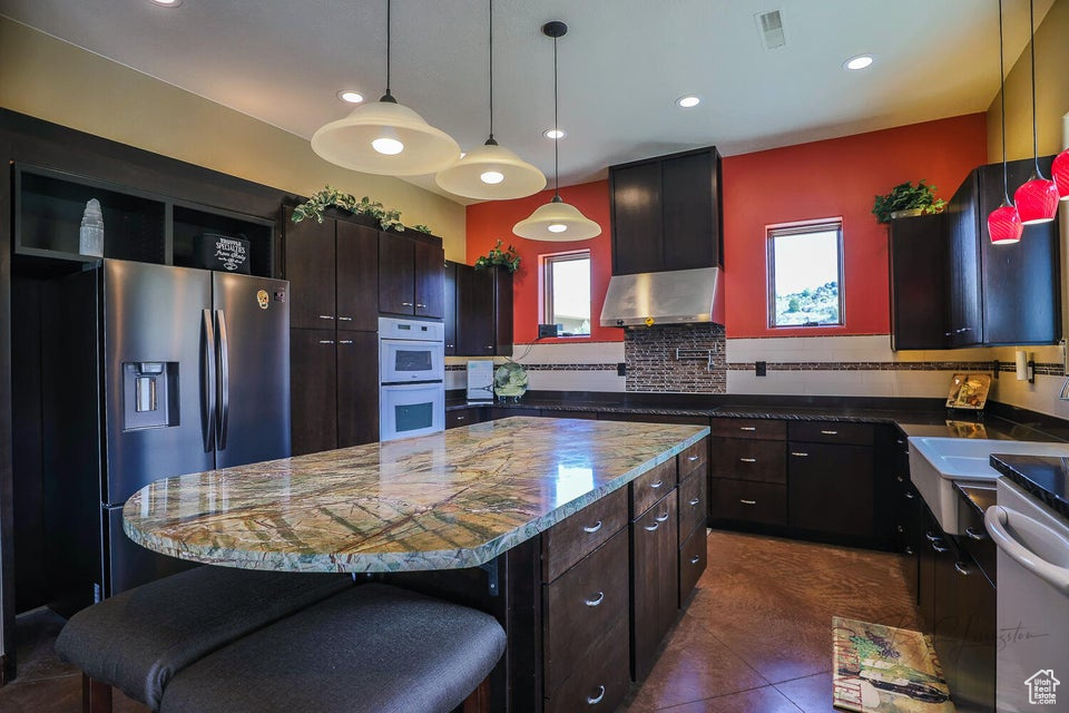 Kitchen with a center island, pendant lighting, a breakfast bar, tasteful backsplash, and dark tile flooring