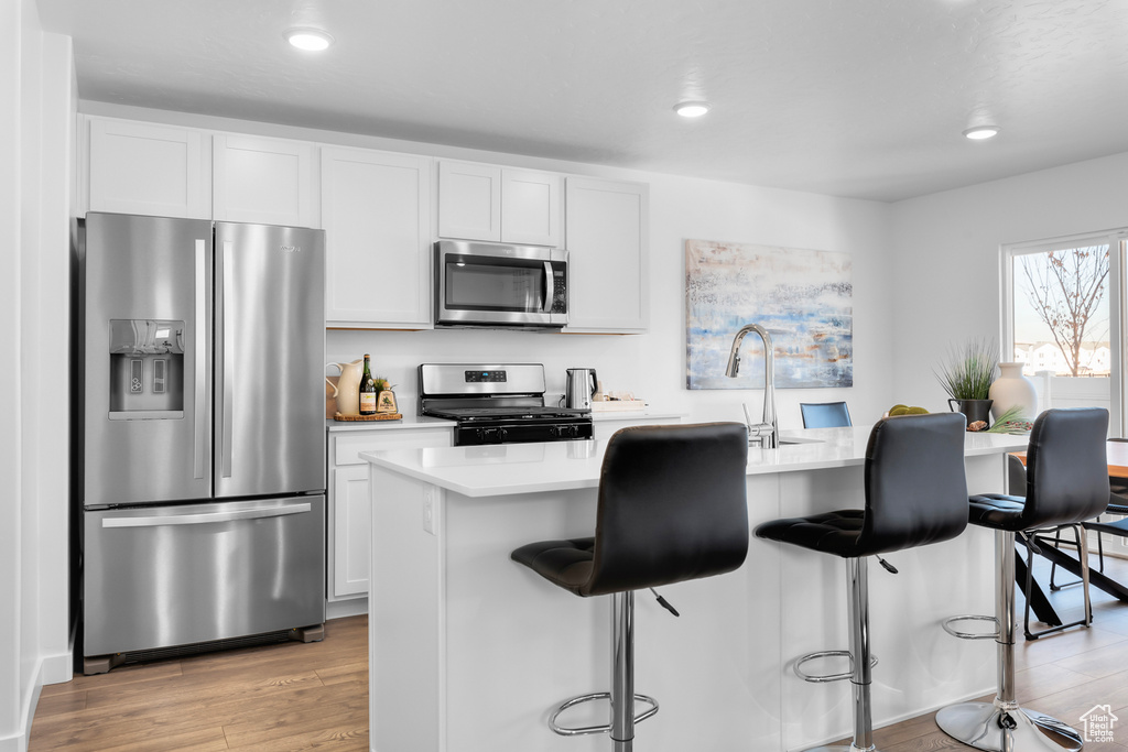 Kitchen with appliances with stainless steel finishes, light hardwood / wood-style floors, white cabinetry, a center island, and a breakfast bar