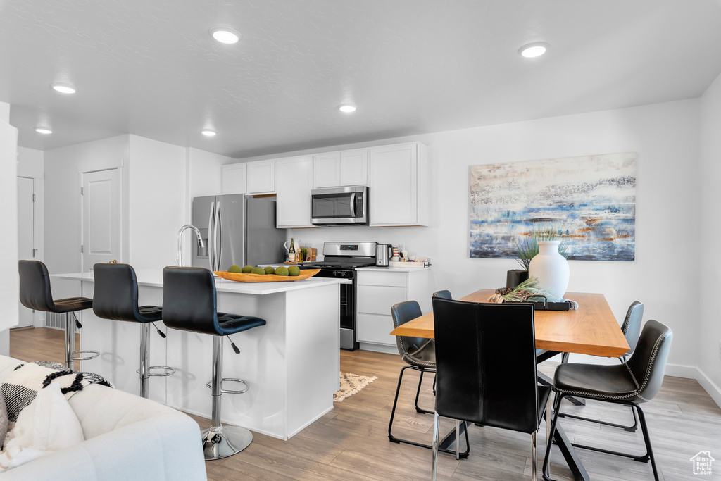 Kitchen featuring white cabinets, light hardwood / wood-style flooring, a kitchen breakfast bar, and stainless steel appliances