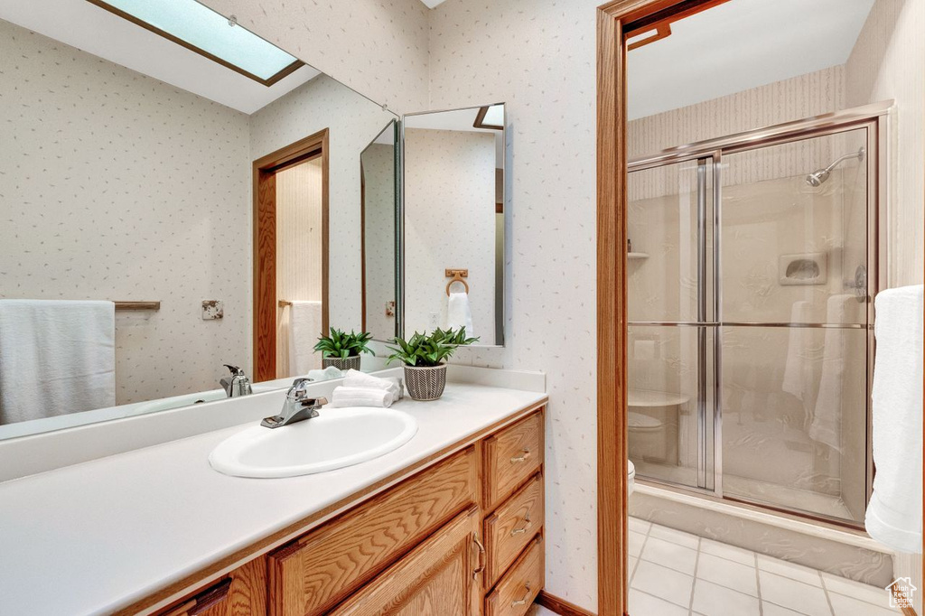 Bathroom with a skylight, large vanity, tile floors, toilet, and a shower with door