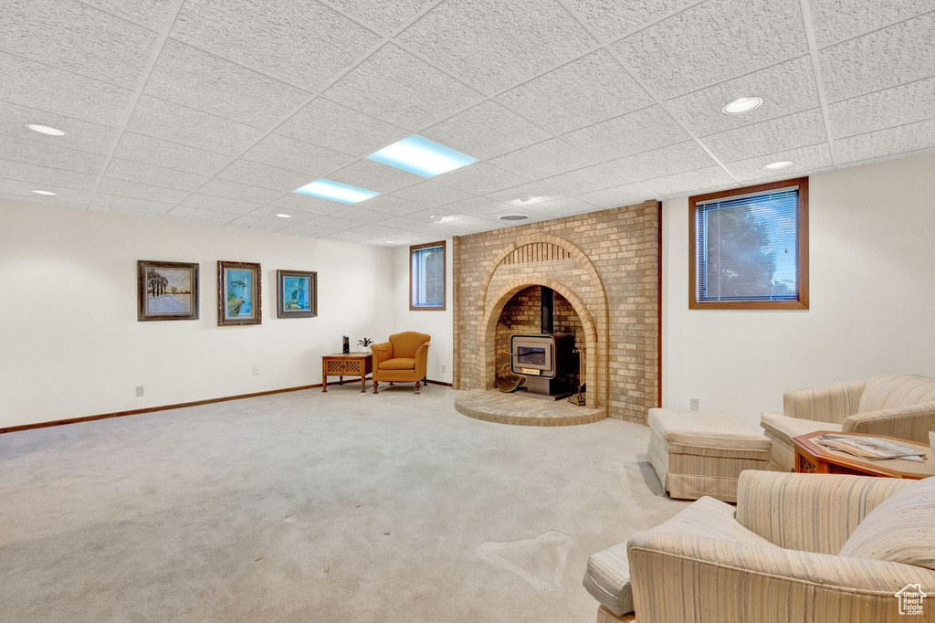 Living room featuring a drop ceiling, a wood stove, carpet, and brick wall