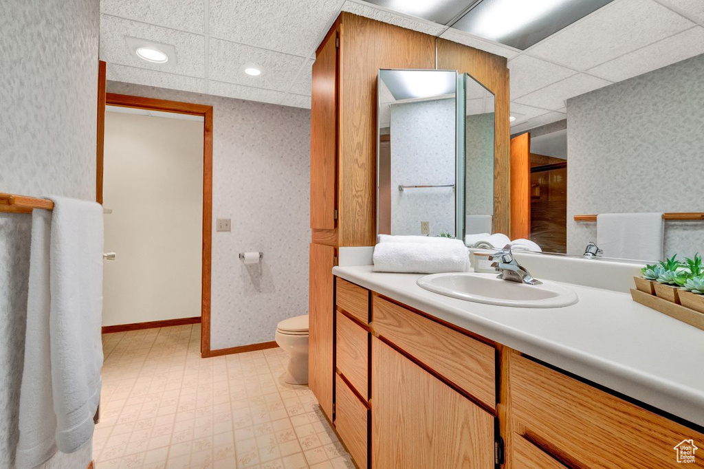 Bathroom with a drop ceiling, large vanity, tile floors, and toilet
