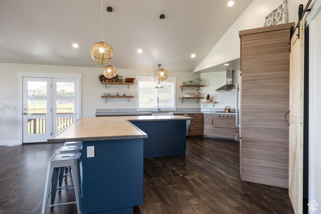 Kitchen featuring plenty of natural light, wall chimney range hood, a barn door, and a breakfast bar area