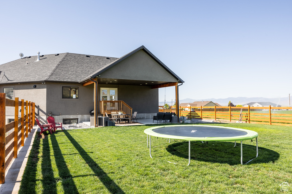 Back of house featuring a mountain view, a trampoline, and a lawn