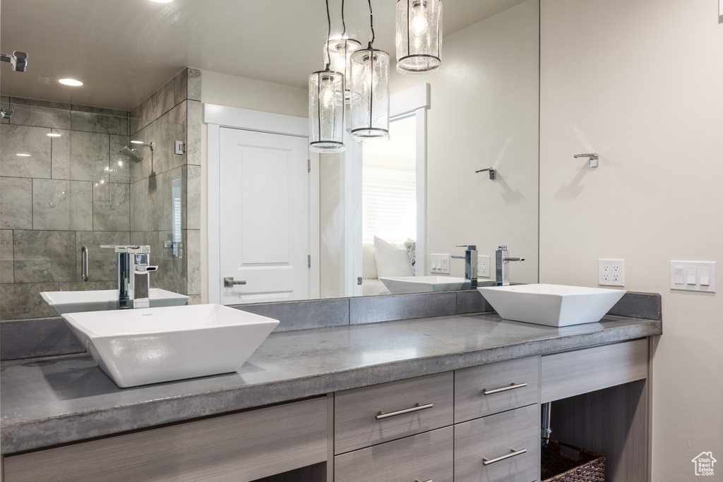 Bathroom featuring a shower with door, vanity with extensive cabinet space, and dual sinks