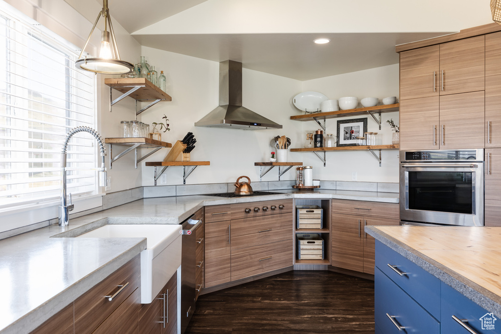Kitchen with stainless steel appliances, dark hardwood / wood-style flooring, wall chimney range hood, sink, and pendant lighting