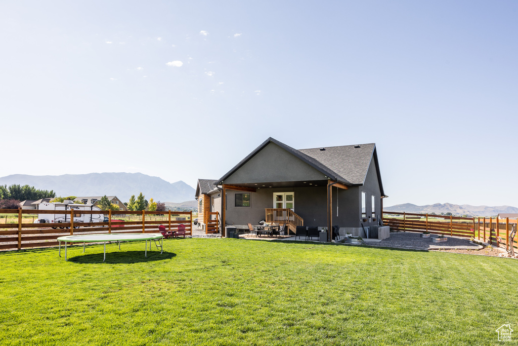 Back of property with a patio, a mountain view, a trampoline, and a lawn