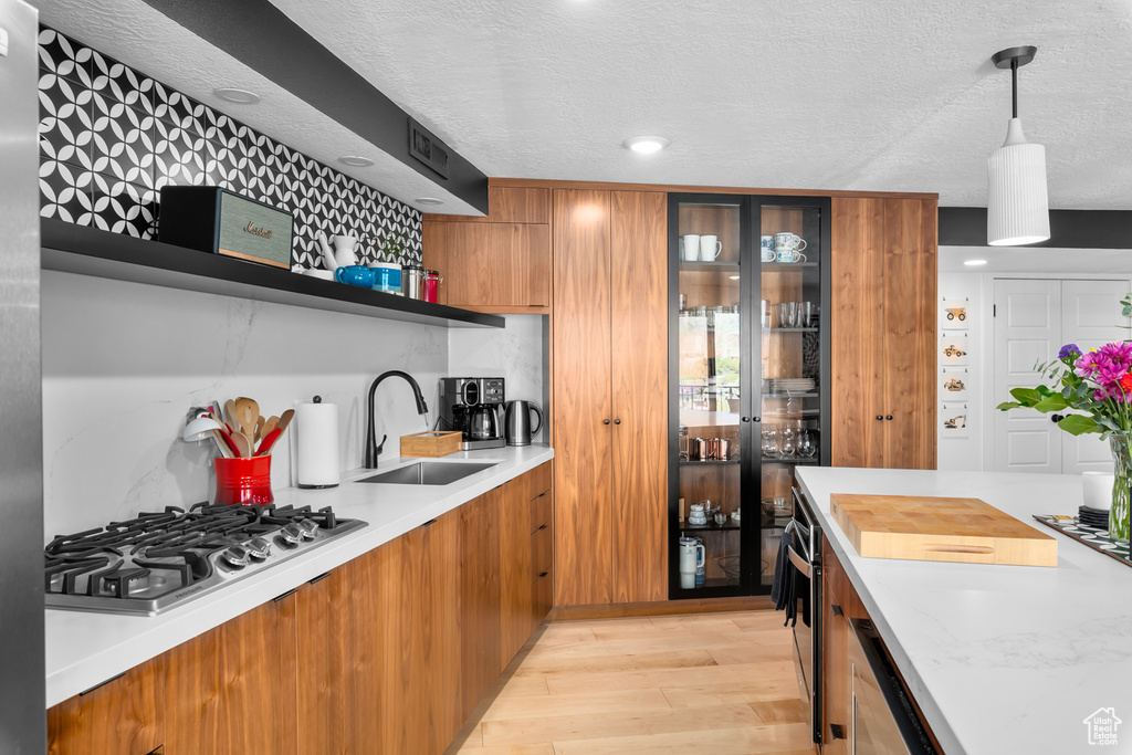 Kitchen with stainless steel gas stovetop, sink, tasteful backsplash, light wood-type flooring, and pendant lighting