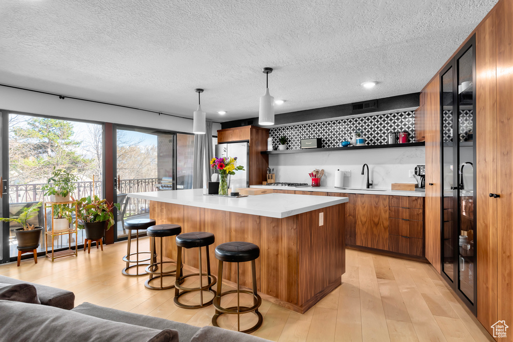Kitchen with a center island, pendant lighting, a breakfast bar, light hardwood / wood-style floors, and stainless steel fridge