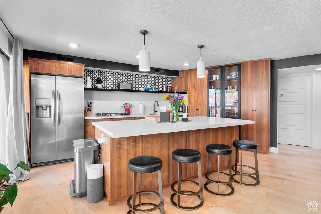 Kitchen with decorative light fixtures, a kitchen island, a breakfast bar area, stainless steel appliances, and light hardwood / wood-style floors
