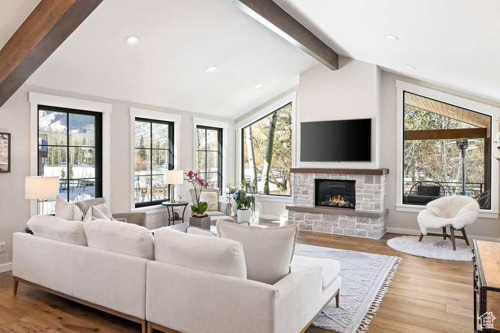 Living room featuring a wealth of natural light, lofted ceiling with beams, light wood-type flooring, and a stone fireplace