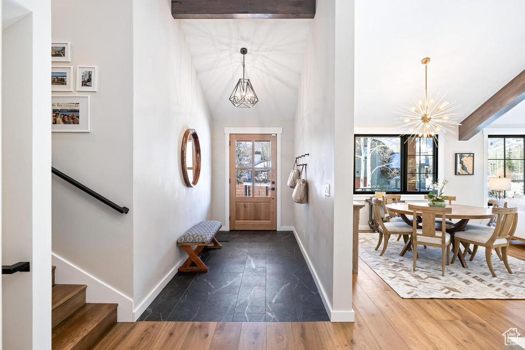 Foyer entrance featuring dark tile flooring, lofted ceiling with beams, and a chandelier