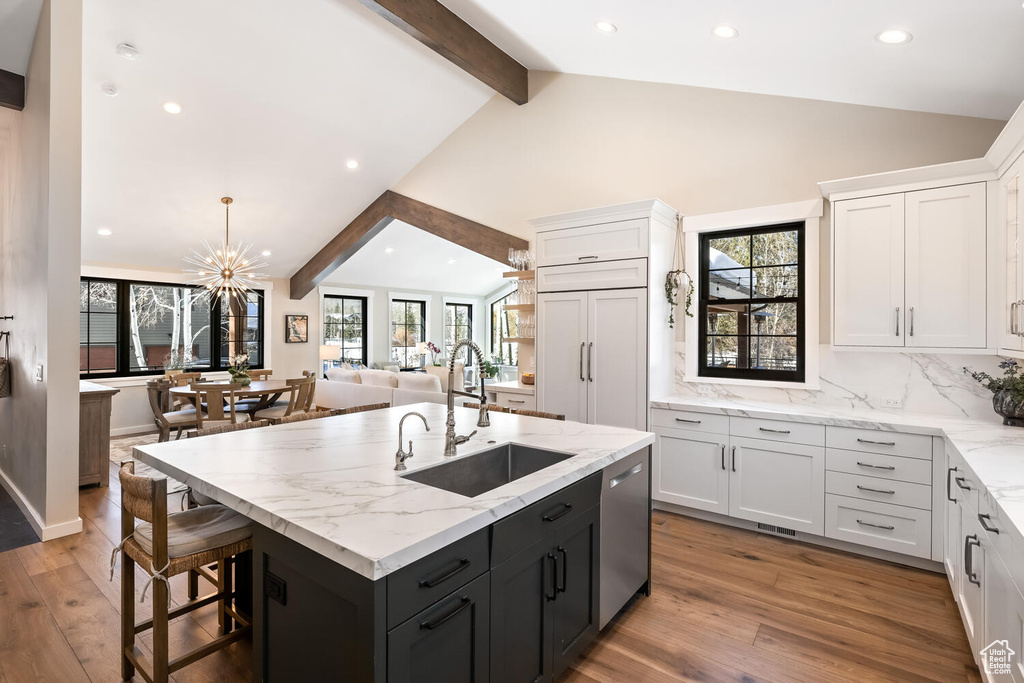 Kitchen with light stone counters, a breakfast bar, vaulted ceiling with beams, sink, and white cabinetry