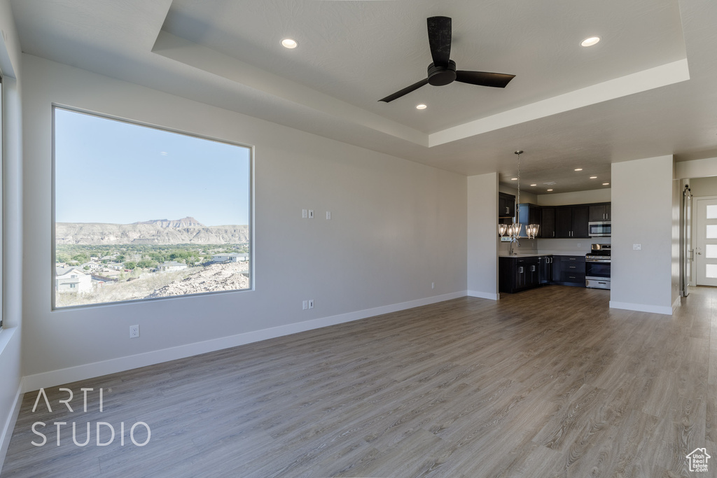 Unfurnished living room with a raised ceiling, wood-type flooring, ceiling fan with notable chandelier, a mountain view, and sink