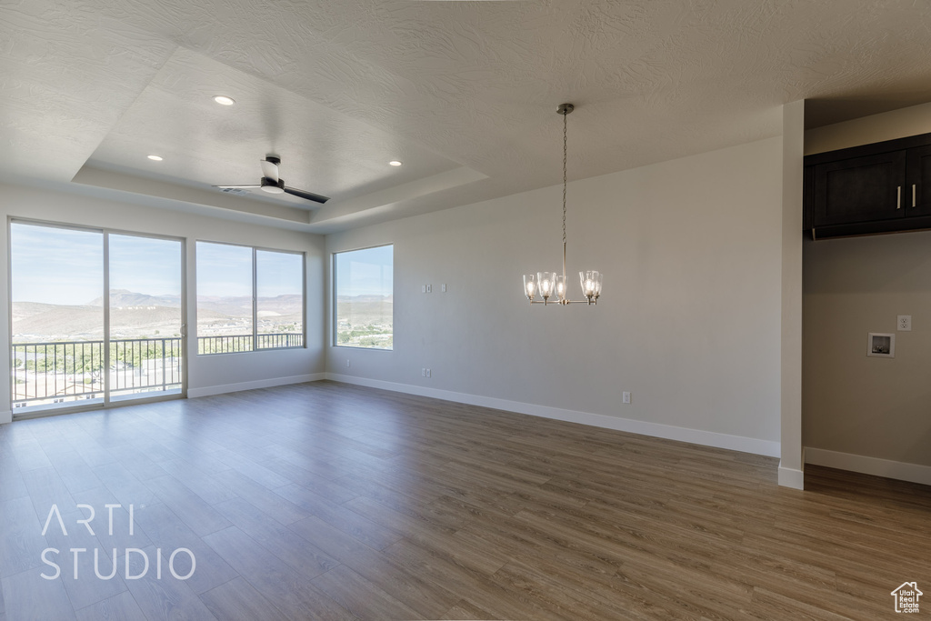 Empty room with a textured ceiling, a tray ceiling, wood-type flooring, ceiling fan with notable chandelier, and a mountain view