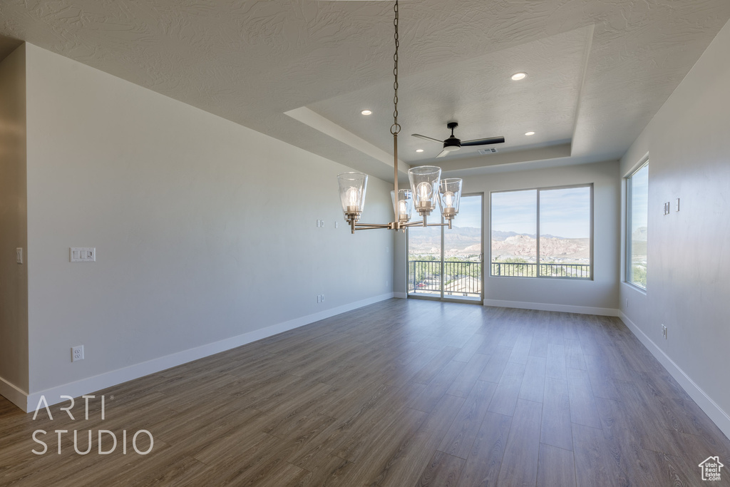 Unfurnished dining area with dark hardwood / wood-style floors, a textured ceiling, a tray ceiling, and ceiling fan with notable chandelier