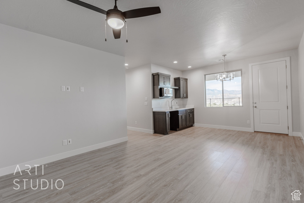 Unfurnished living room with sink, light wood-type flooring, and ceiling fan with notable chandelier