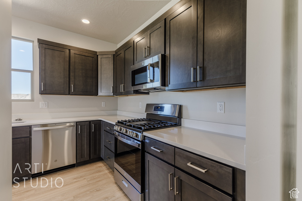 Kitchen with appliances with stainless steel finishes, dark brown cabinetry, a textured ceiling, and light hardwood / wood-style floors